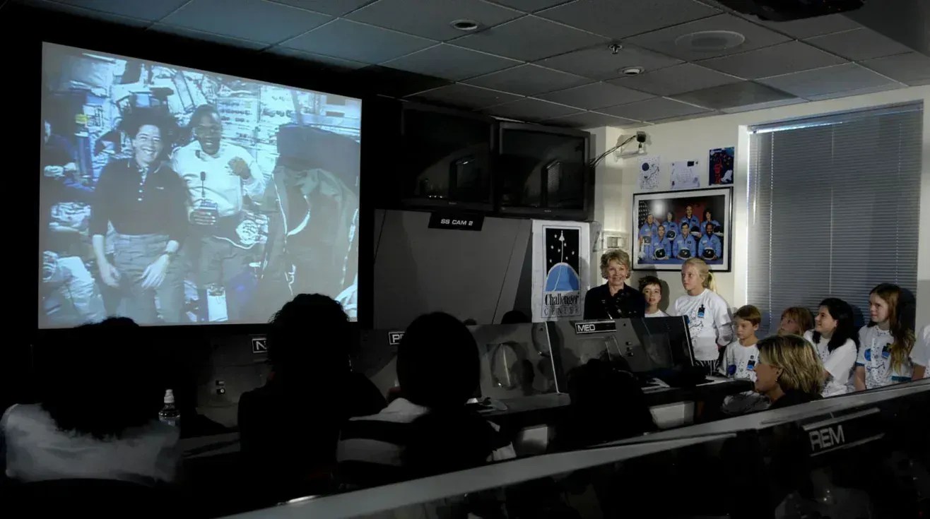 A Dra. June Scobee Rodgers, fundadora do Challenger Center, cumprimenta os astronautas Barbara Morgan e Benjamin Drew Jr. durante uma transmissão ao vivo para os alunos do centro em 16 de agosto de 2007 • Paul E. Alers/Nasa