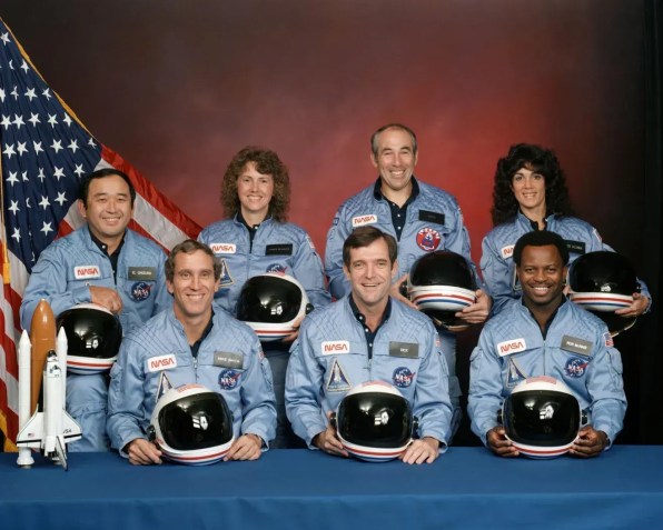 Membros da tripulação do Challenger (da esquerda para a direita, na primeira fila): Michael J. Smith, Francis R. (Dick) Scobee e Ronald E. McNair; (na segunda fila, da esquerda para a direita): Ellison S. Onizuka, Sharon Christa McAuliffe, Gregory Jarvis e Judith A. Resnik posam juntos em dezembro de 1985 • Nasa