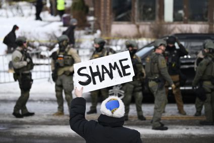 Um espectador segura uma placa com a palavra "Vergonha" enquanto policiais trabalham no local após uma mulher ser morta a tiros por um agente de imigração em 7 de janeiro de 2026 em Minneapolis, Minnesota.