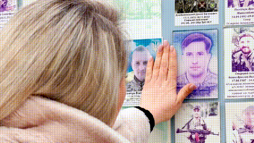 Juliia Seliutina toca o retrato do marido em muro memorial de Kiev. • CNN