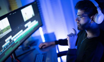 Young man engaged in video editing at a modern workstation surrounded by blue lighting