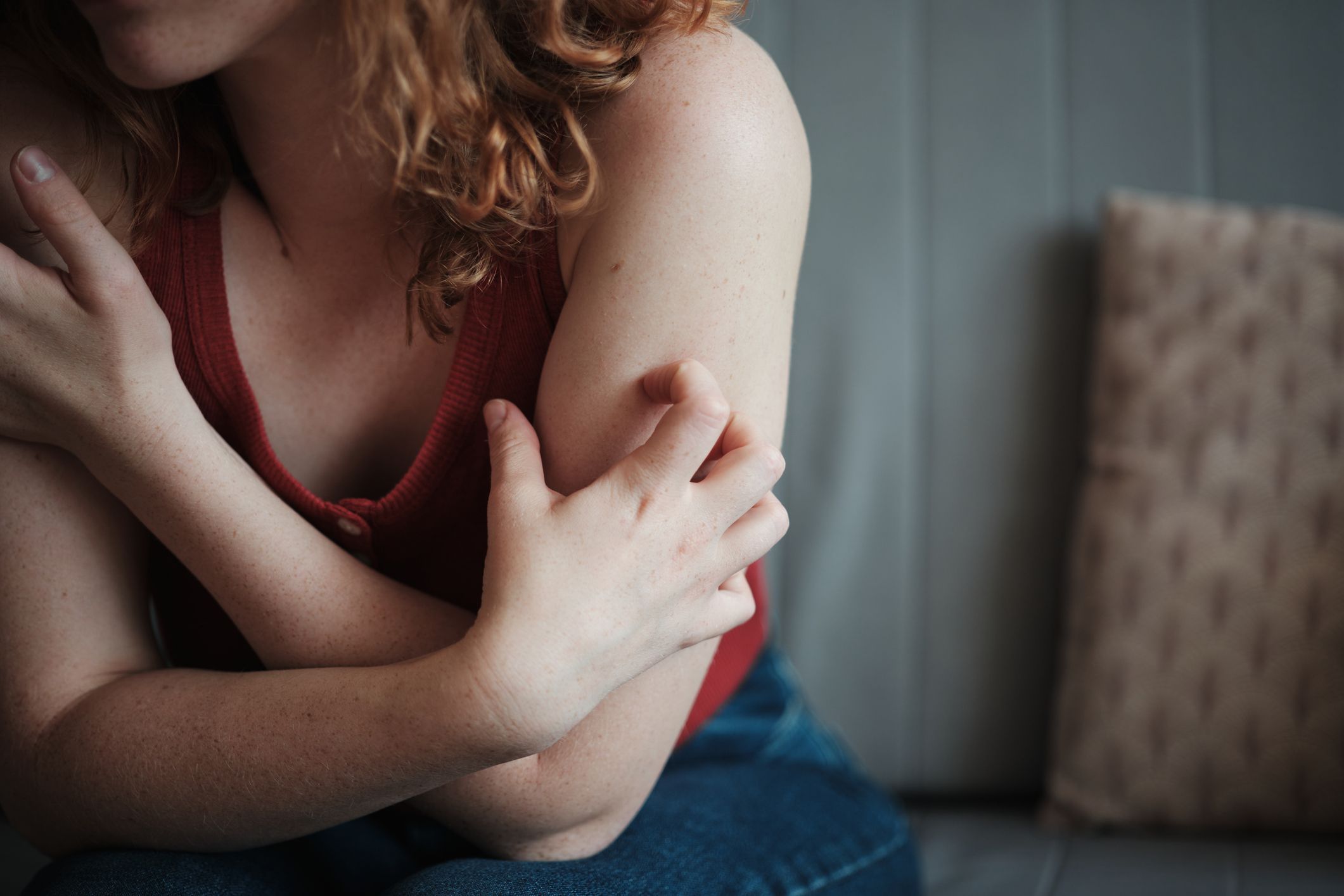 Close up of nervous stressed woman itching her skin, sitting on sofa at home, feeling anxious. Stress Rash
