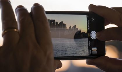 pessoa-fotografando-paisagem-urbana-com-smartphone-ao-por-do-sol-opera-house-e-arranha-ceus-ao-fundo-foto-mobile