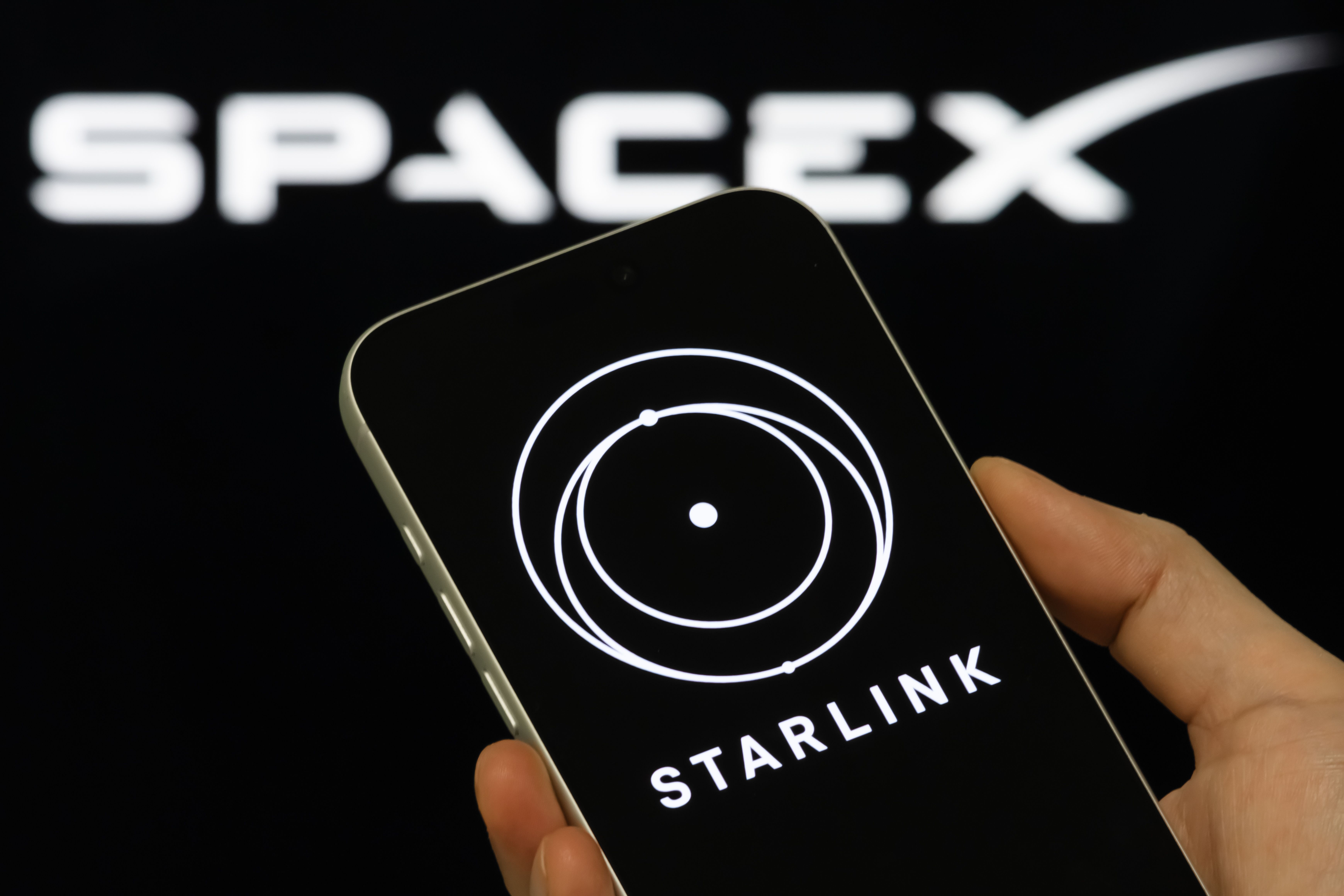 Starlink Logo Shown On Smartphone With SpaceX Branding In Background