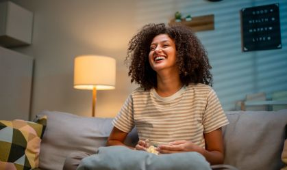 Latina woman eating popcorn and watching movie on television at home at night. Attractive girl sitting on sofa feeling happy and excited, watch series on TV show. Activity lifestyles concept.