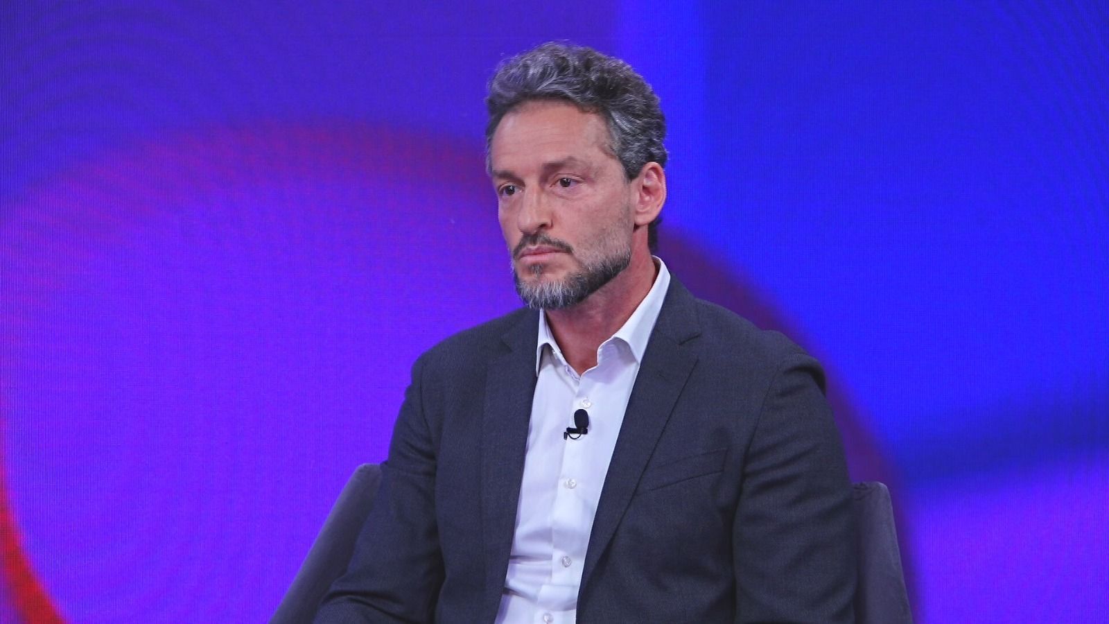 André Lavor, presidente da Binatural, sentado em um fundo azulado, com um terno cinza.