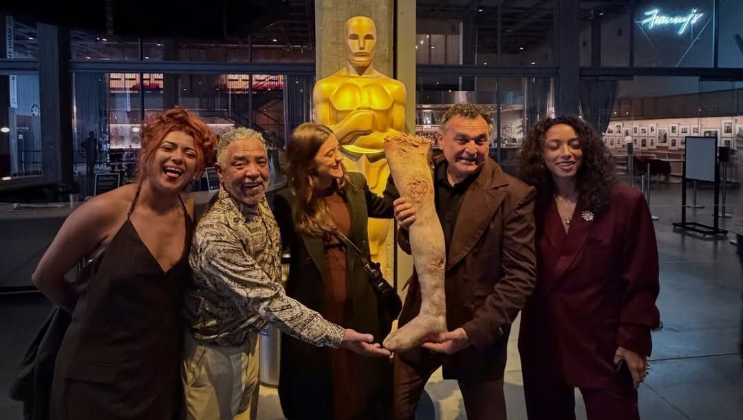 Elenco de "O Agente Secreto" segurando uma Perna Cabeluda