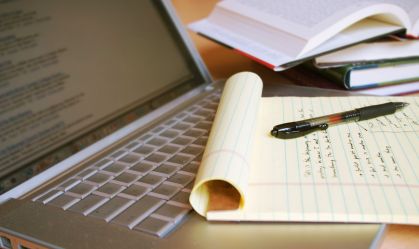 Laptop computer with books, pen and yellow legal pad