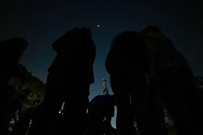 Pessoas se reúnem perto de um telescópio para observar a lua cheia de sangue em Caracas, Venezuela, em março de 2025 • Juan Barreto/AFP/Getty Images