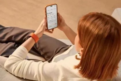 Mulher ruiva de cabelo curto e liso sentada, segurando o celular com as duas mãos enquanto utiliza serviços financeiros pelo aplicativo do Inter.