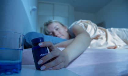 Woman reaching for melatonin bottle during bedtime