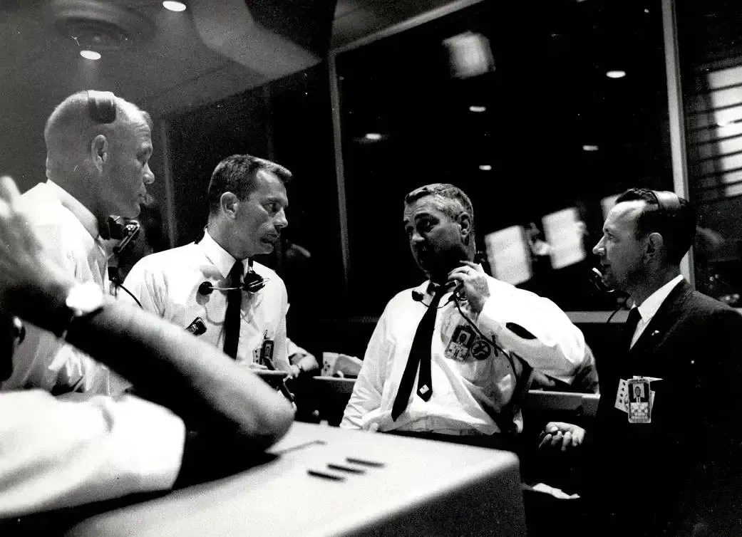 Da esquerda para a direita, os astronautas John Glenn e Donald K. Slayton, Walter C. Williams, diretor associado de operações do Projeto Mercury, e Christopher Kraft, diretor de voo, conversam dentro da Área de Controle de Voo. • Nasa