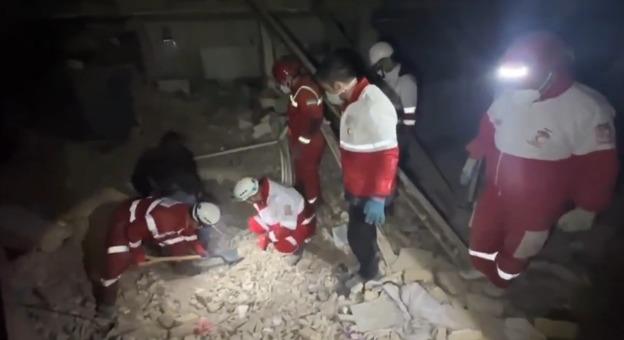 Equipes de resgate do Crescente Vermelho Iraniano vasculham escombros em área residencial de Teerã após ataque aéreo.