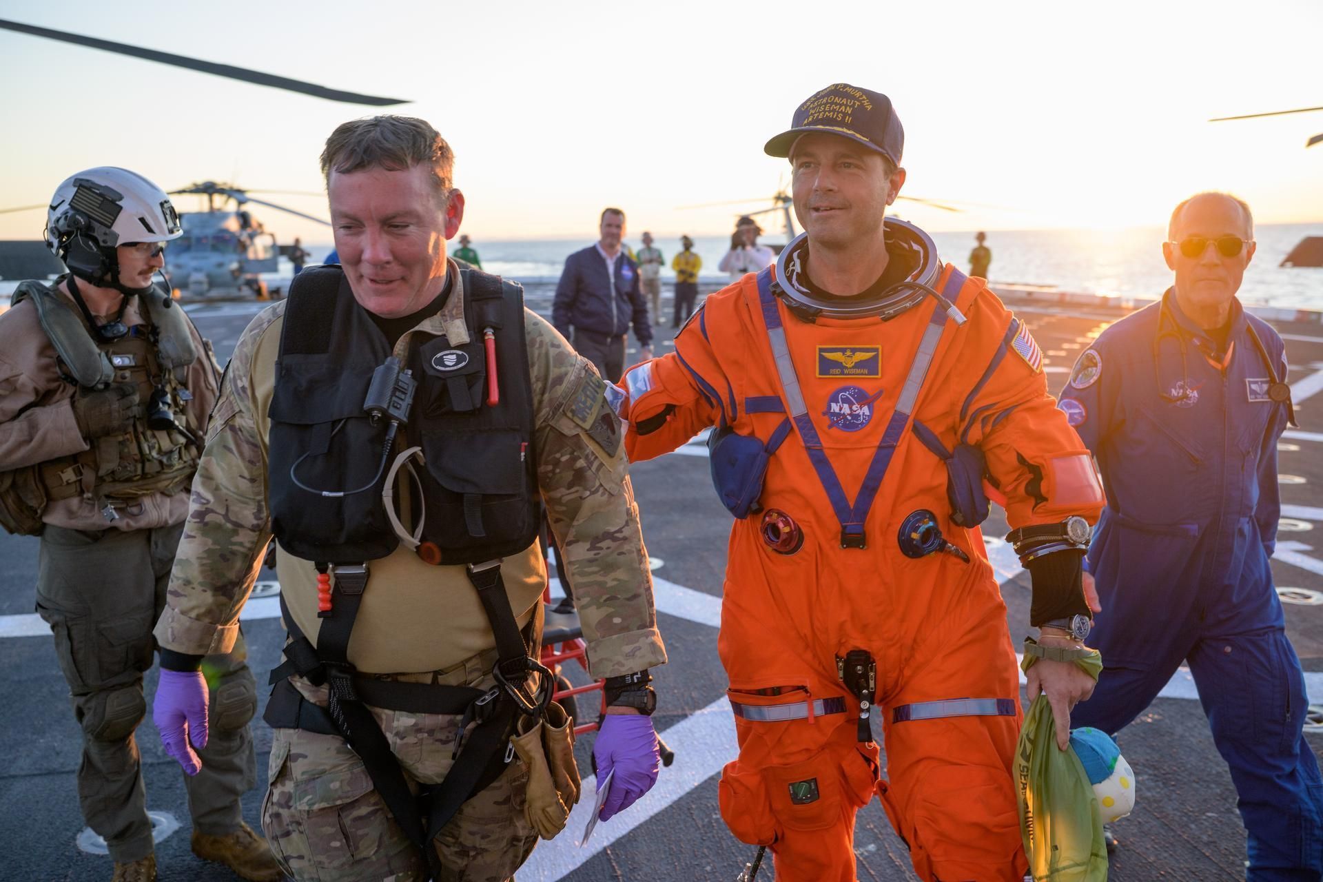 O astronauta Reid Wiseman, comandante da Artemis II, é auxiliado a sair do convés de voo após chegar a bordo do USS John P. Murtha