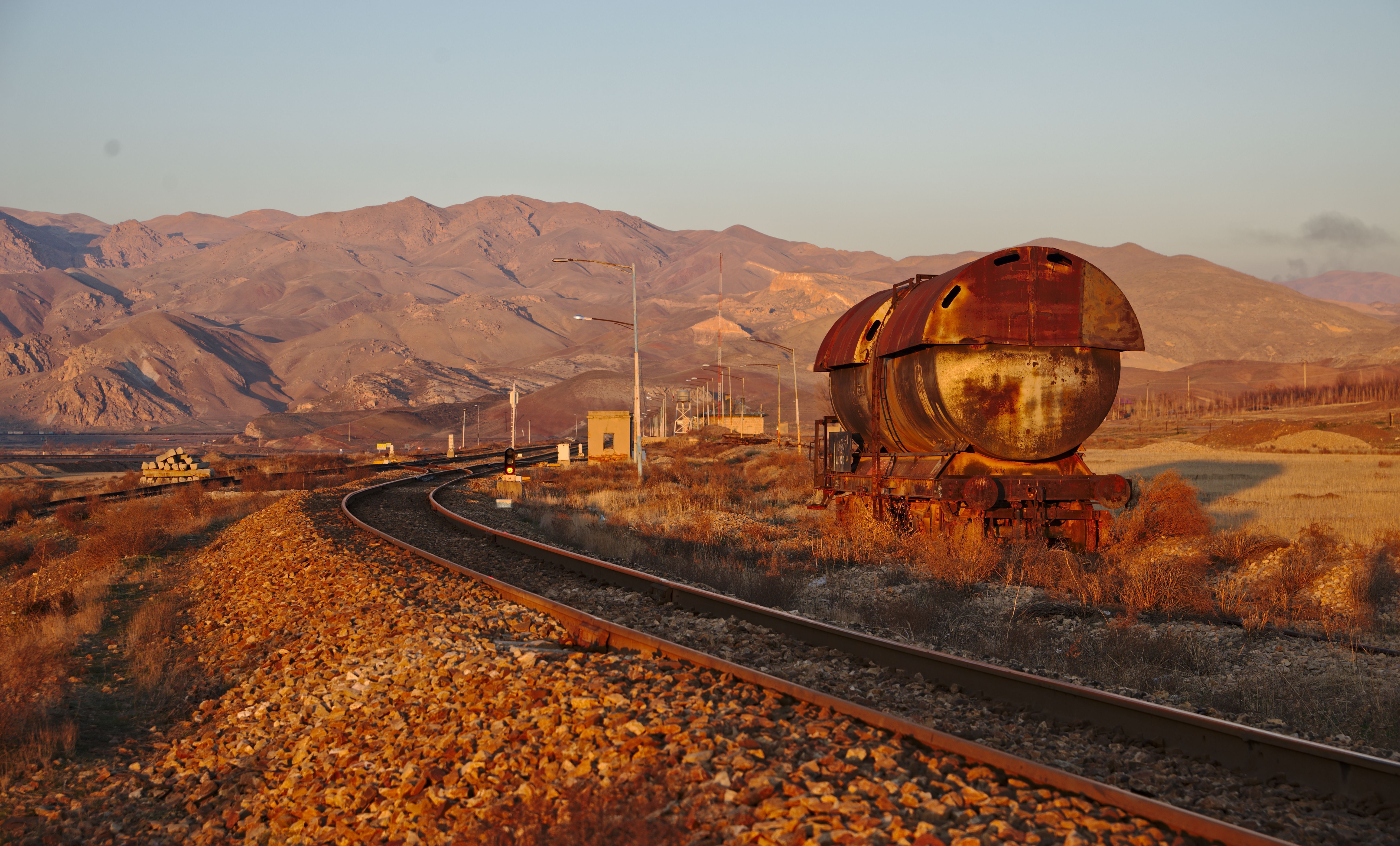 Railroad Tracks And Old Rusty Locomotive In Desert Against Clear Sky At Sunset And Golden Hour