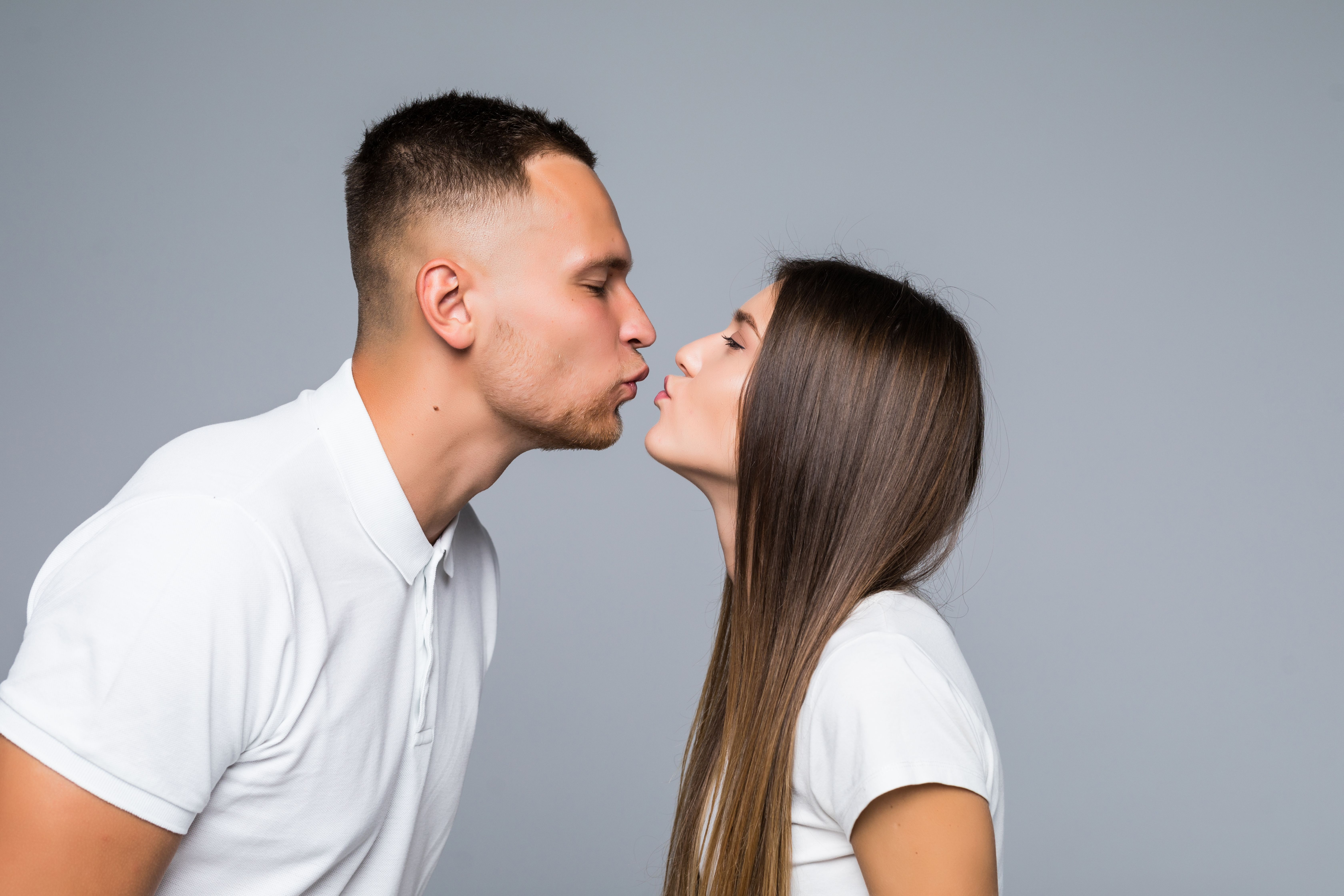 Close up portrait of boyfriend kissing girlfriend isolated on grey