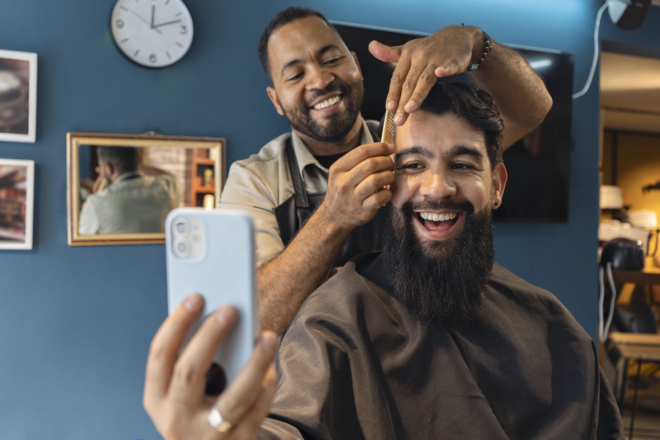 Smiling barber and customer in the barbershop watching a video on a smartphone.