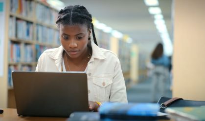 Black woman, student and laptop in library for education, research or studying in school. Girl, computer or reading in university for problem solving, assessment planning or course information on web