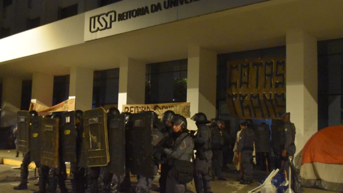 Fachada do prédio da Reitoria e Administração Central da USP em São Paulo com carros de polícia estacionados na frente.