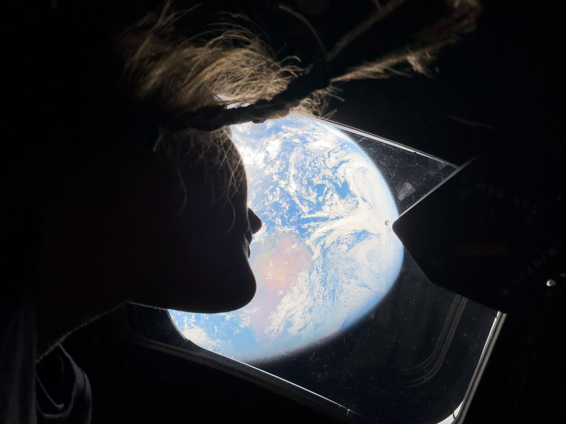 A astronauta da NASA e especialista da missão Artemis II, Christina Koch, olha através de uma das janelas da cabine principal da espaçonave Orion, observando a Terra enquanto a tripulação viaja em direção à Lua • Nasa