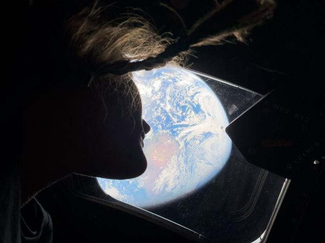 A astronauta da NASA e especialista da missão Artemis II, Christina Koch, olha através de uma das janelas da cabine principal da espaçonave Orion, observando a Terra enquanto a tripulação viaja em direção à Lua • Nasa
