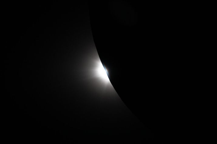 Capturada pela sonda Orion perto do fim do sobrevoo lunar da missão Artemis II em 6 de abril, esta imagem mostra o Sol começando a surgir por trás da Lua enquanto o eclipse transita para fora da totalidade. Apenas uma parte da Lua é visível na imagem, sua borda curva revelando uma faixa brilhante de luz solar retornando após quase uma hora de escuridão. Nos momentos finais do eclipse observados pela tripulação, a luz que reaparece cria um forte contraste com a silhueta da Lua e revela a topografia lunar normalmente não visível ao longo do limbo lunar. Esta fase fugaz captura o alinhamento dinâmico do Sol, da Lua e da sonda enquanto a Orion continua sua jornada de volta do lado oculto da Lua. • Nasa