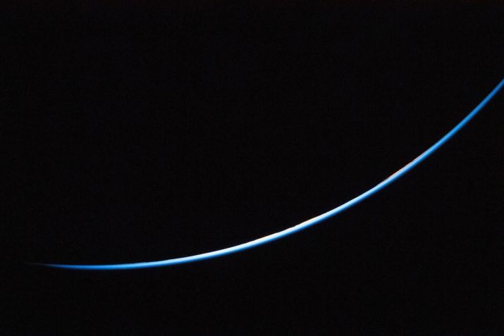 Uma pequena faixa da borda da Terra brilha intensamente contra a vasta escuridão do espaço. • Nasa