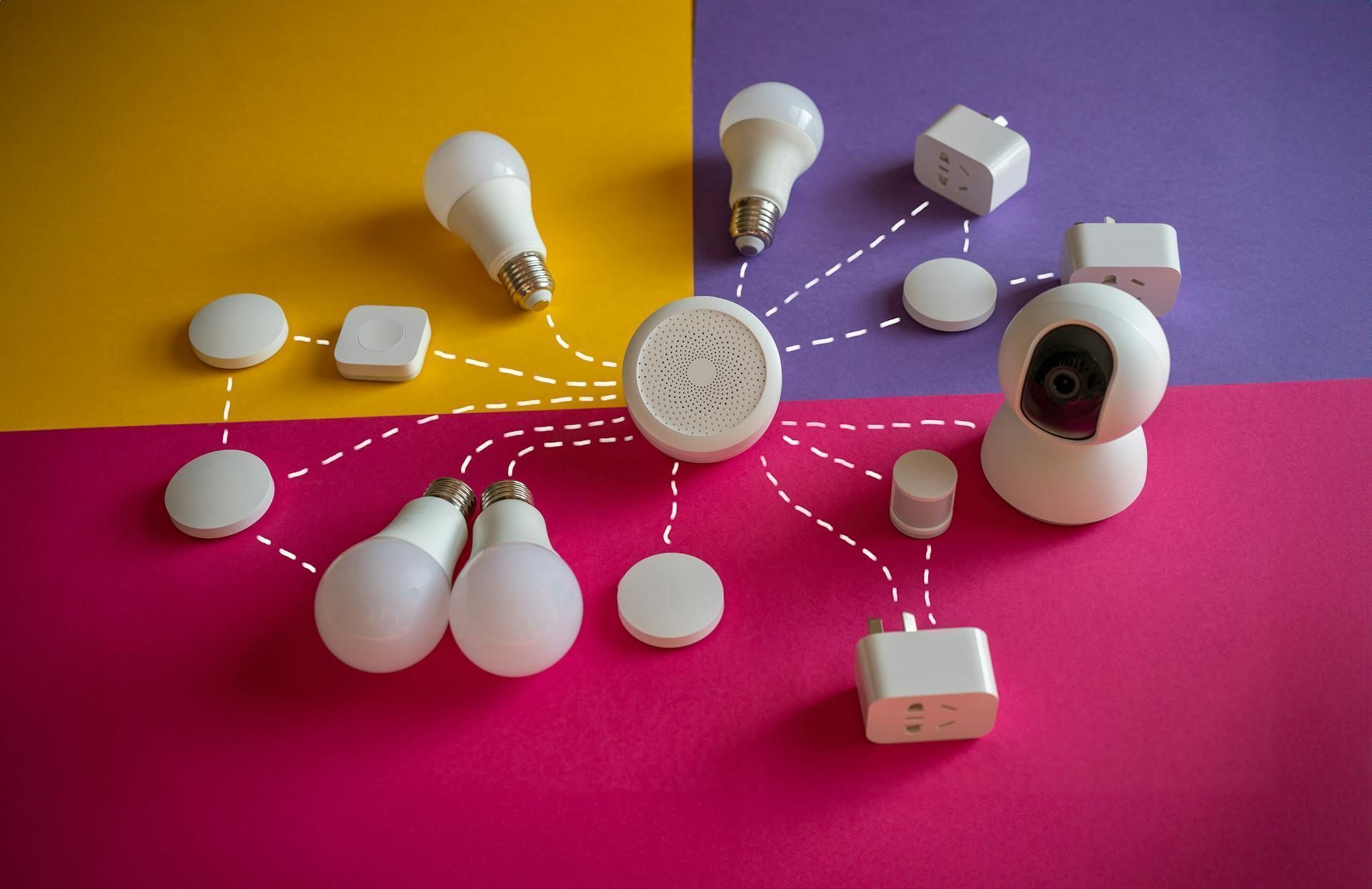 lampada-tomada-camera-inteligente-produtos-de-smart-home-conectados-com-pontinhos-em-uma-mesa-de-cores-amarelo-vermelho-e-roxo