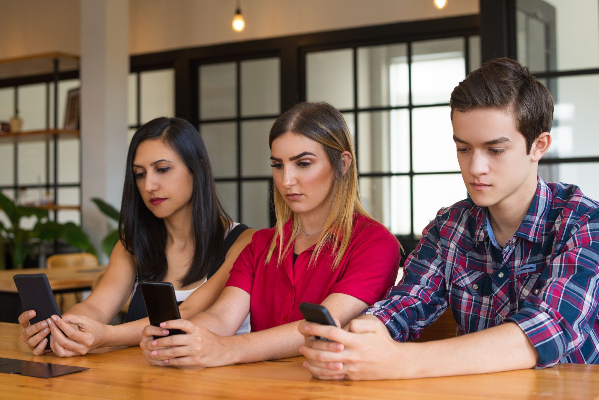 três-adolescentes-sentados-lado-a-lado-usando-seus-celulares-sem-se-falar
