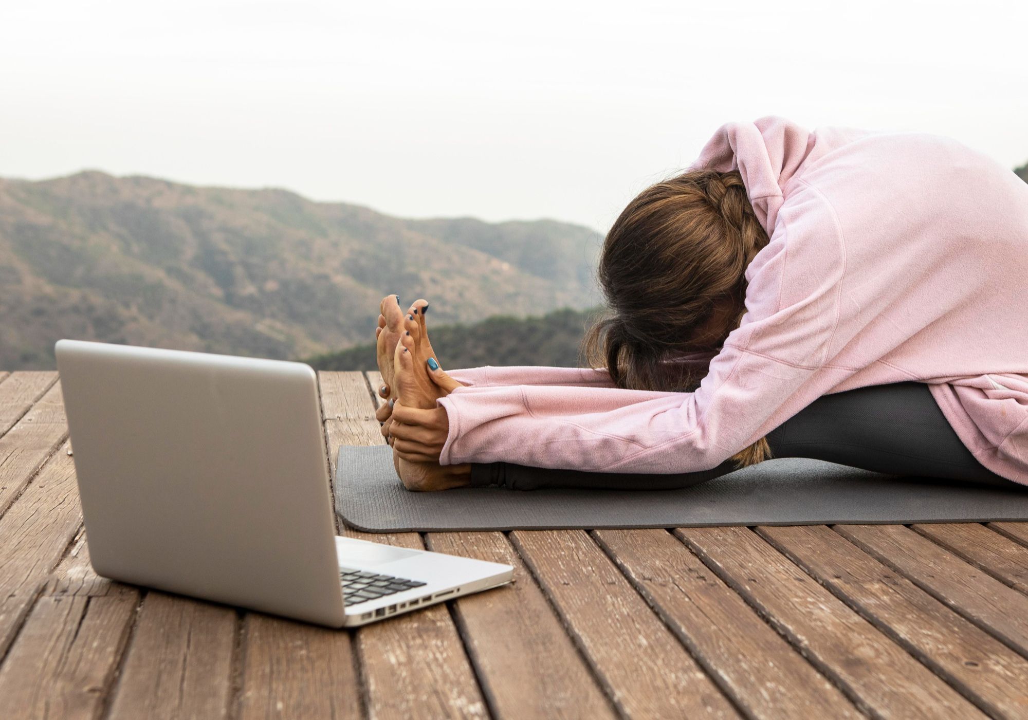 mulher-com-laptop-praticando-yoga-no-alto-de-montanha