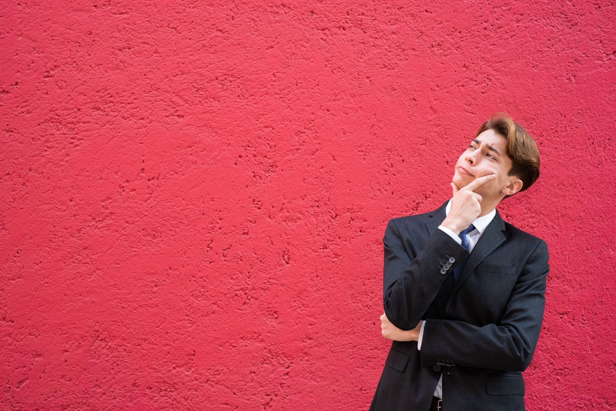 Young Latino man in a suit and tie considering his options, man deep in thought, looking up