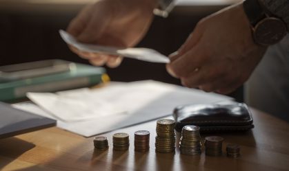 Pessoa compara juros de serviços financeiros, segura dinheiro com as duas mãos e tem uma folha de papel e moedas em cima da mesa na sua frente.