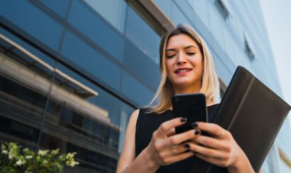 Mulher de blusa preta investindo em ações pelo celular.