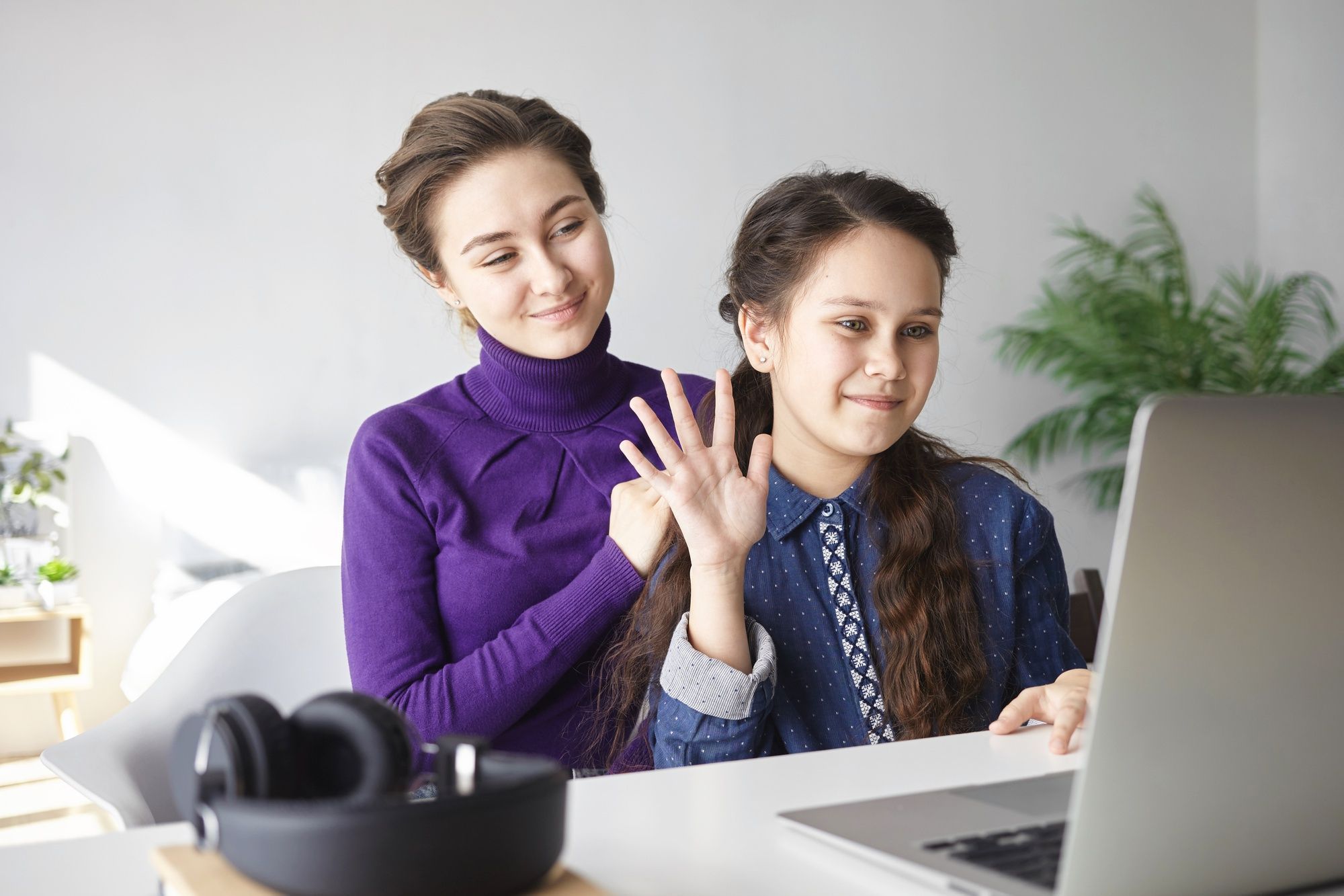 jovem-aluna-acenando-para-tela-de-laptop-com-orientadora-ao-lado