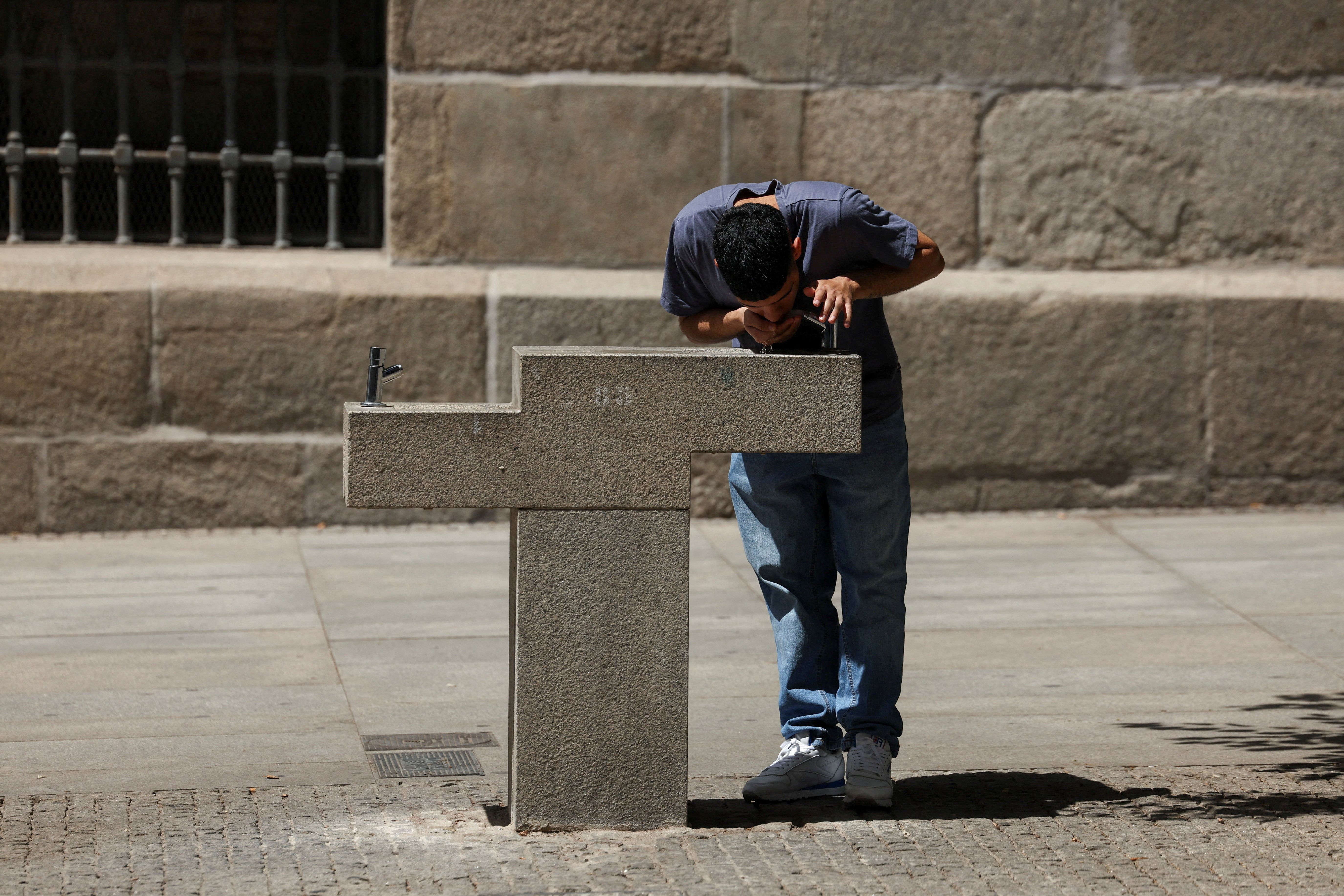 Pessoa bebe água de bebedouro durante onda de calor em Madri