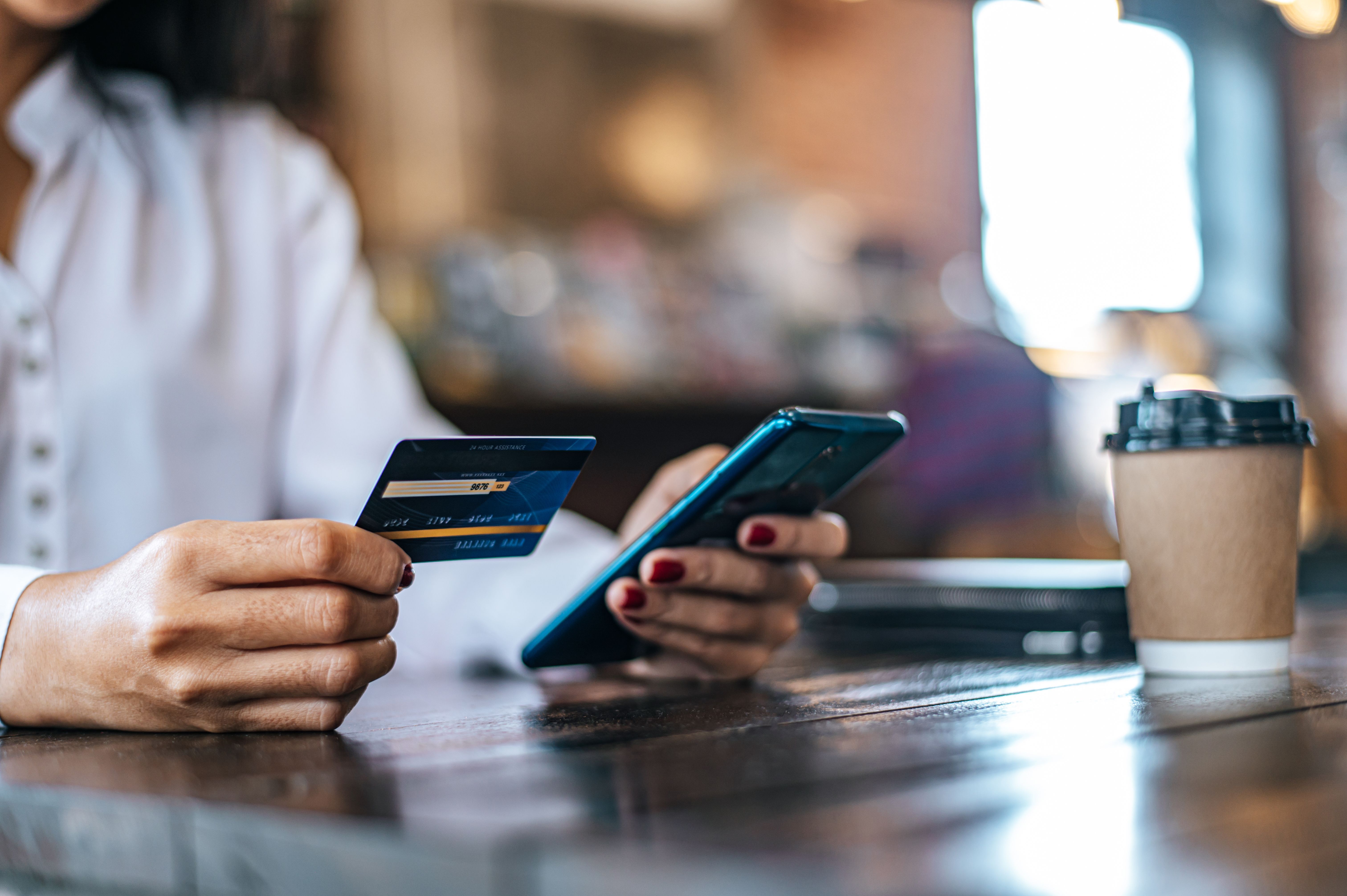 Pessoa usa serviços bancários pelo celular, com o cartão de crédito am uma das mãos.