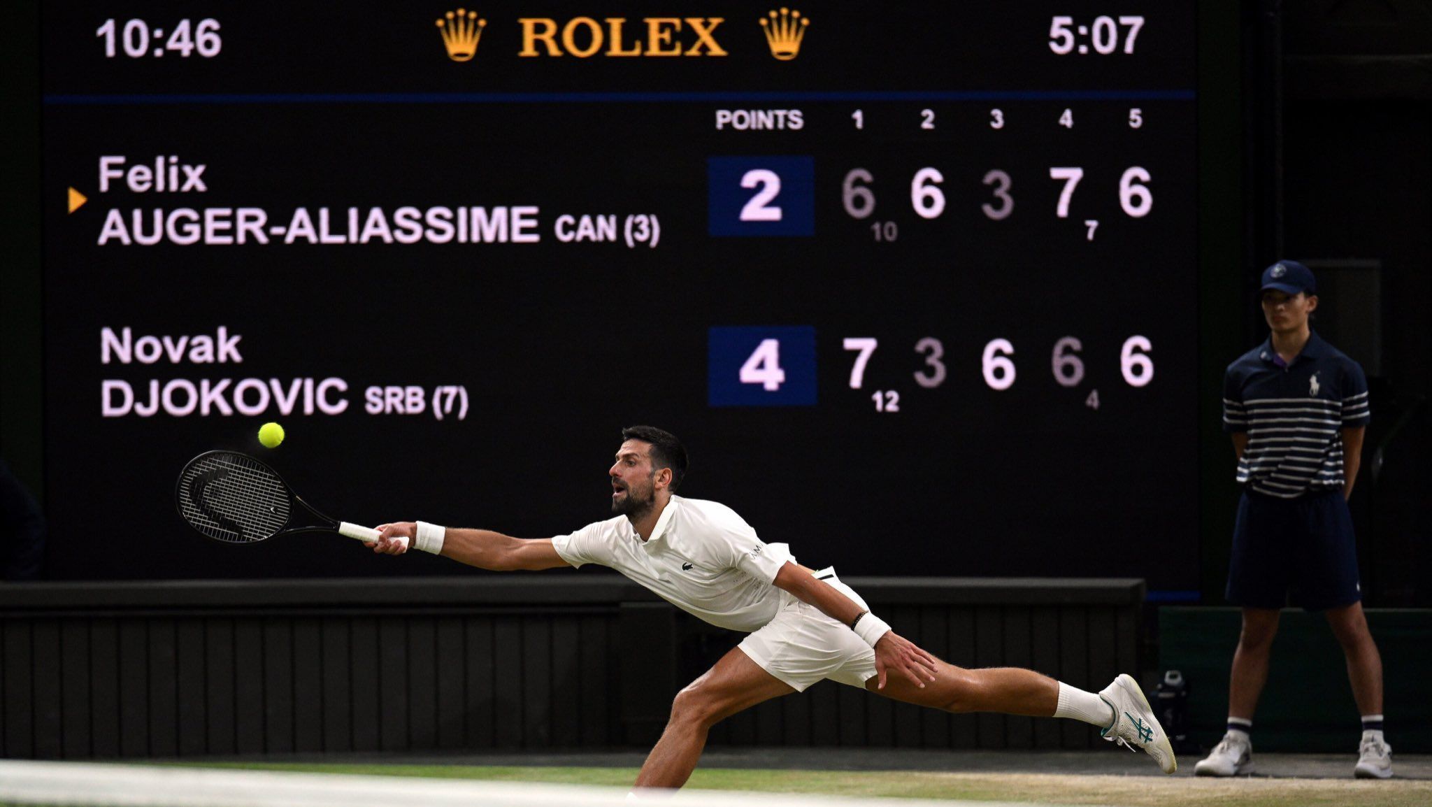 Novak Djokovic na vitória sobre Felix Auger-Aliassime em Wimbledon; atrás dele, o placar mostrando que a partida já tinha passada das cinco horas de duração