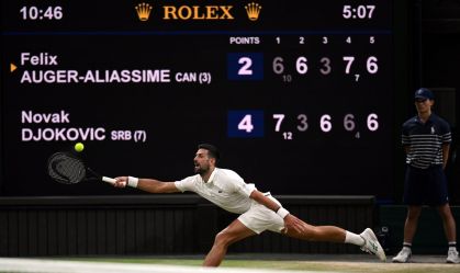 Novak Djokovic na vitória sobre Felix Auger-Aliassime em Wimbledon; atrás dele, o placar mostrando que a partida já tinha passada das cinco horas de duração