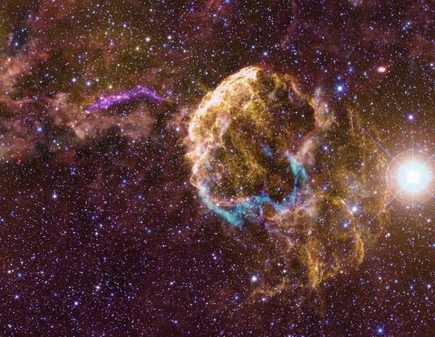 Esta imagem em múltiplas faixas de comprimento de onda mostra o remanescente de supernova da Nebulosa da Água-viva (à direita), a nuvem interestelar com a qual interage e um filamento curvo característico à sua esquerda e acima. O filamento, mostrado aqui tanto em luz visível quanto ultravioleta (UV), é a parte visível de um remanescente de supernova sobreposto, G189.6+3.3, mais proeminente em ondas de rádio e raios X • Nasa