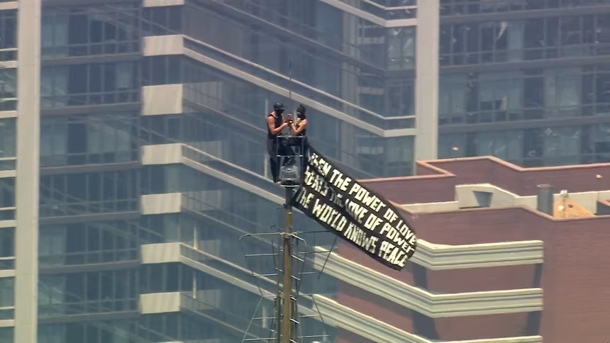 Duas pessoas escalam o topo do Empire State Building carregando uma faixa em 1º de julho de 2026
