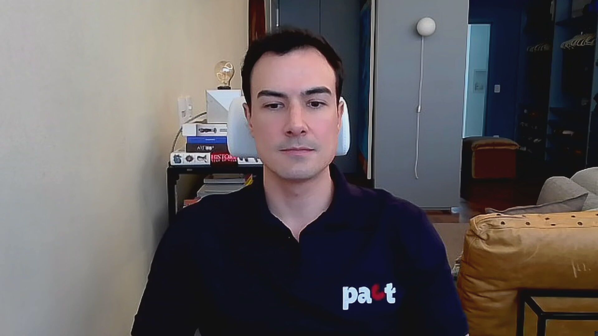 Lucas Pena. CEO da Pact, está sentado em um cadeira. Veste camisa axzul marinho, com o logo da empresa no canto superior direito. Ao fundo, é possívek ver um sofá na cor caramelho e uma mesa com livros