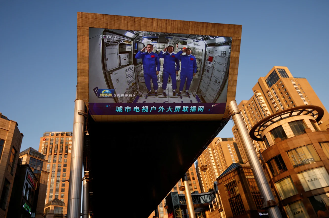Em um shopping center em Pequim, um telão gigante mostra taikonautas prestando continência dentro do módulo central Tianhe da estação espacial chinesa em 2021 • Thomas Peter/Reuters