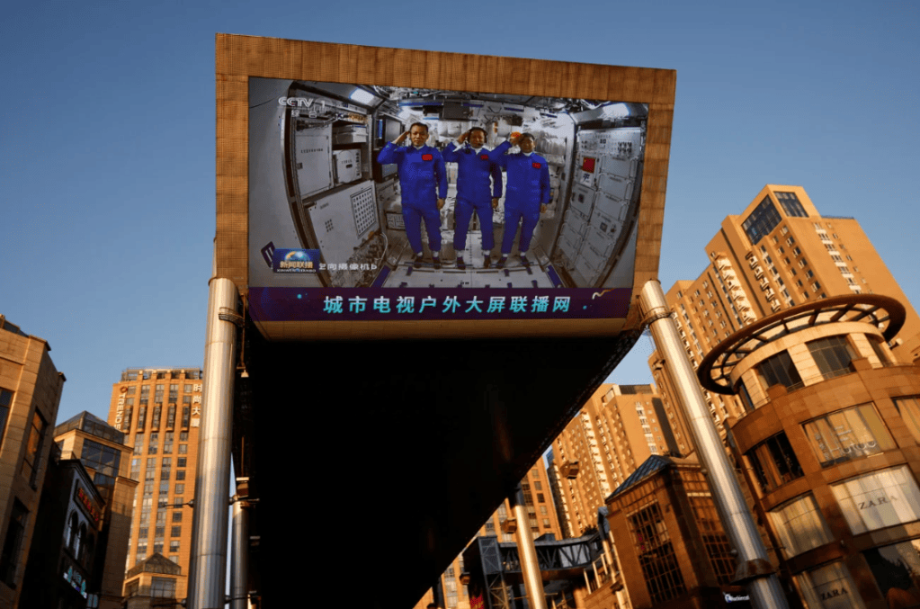 Em um shopping center em Pequim, um telão gigante mostra taikonautas prestando continência dentro do módulo central Tianhe da estação espacial chinesa em 2021 • Thomas Peter/Reuters
