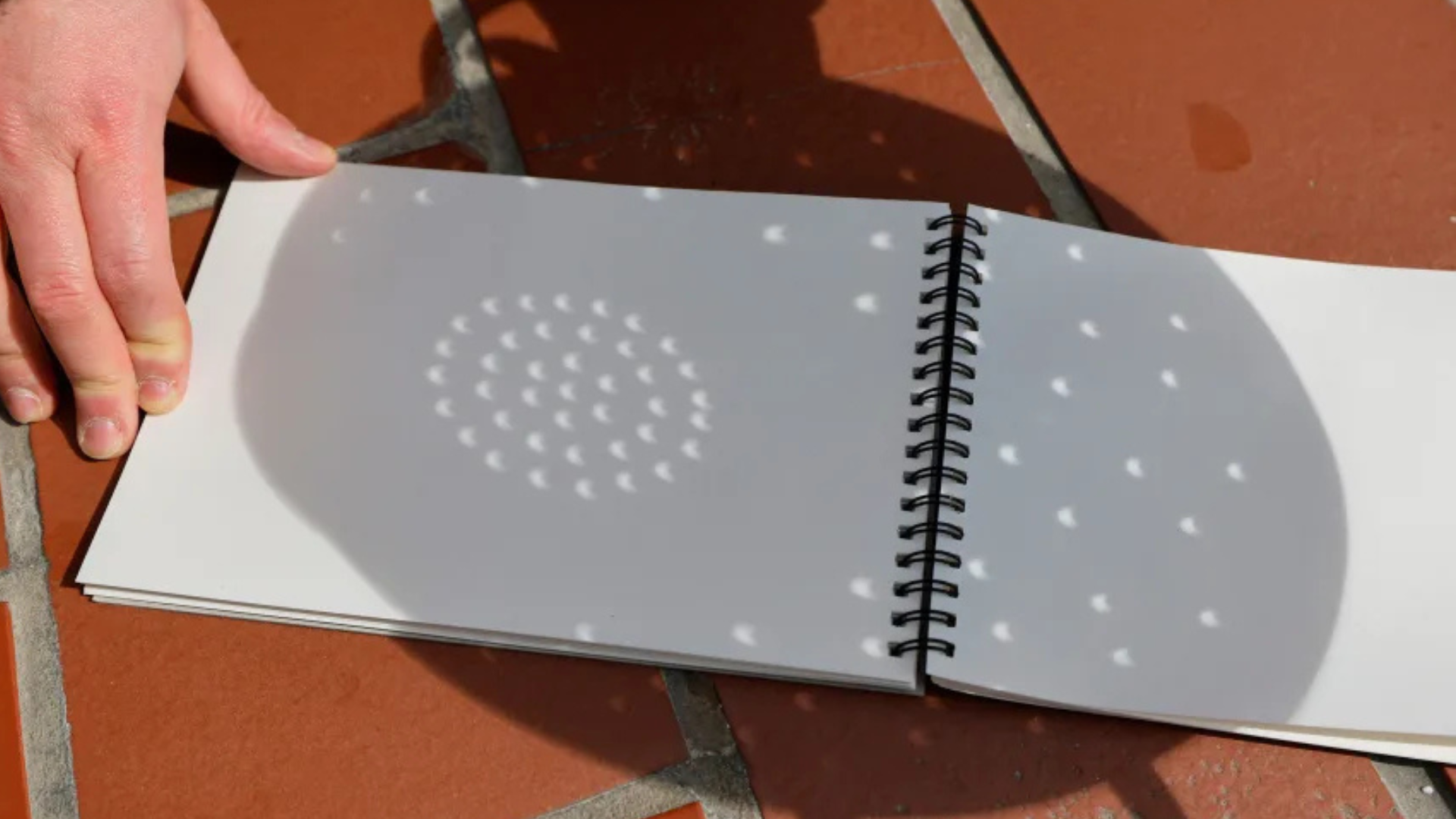 Uma pessoa usa uma peneira e papel para ver a sombra de um eclipse solar parcial. • Michael M. Santiago/Getty Images