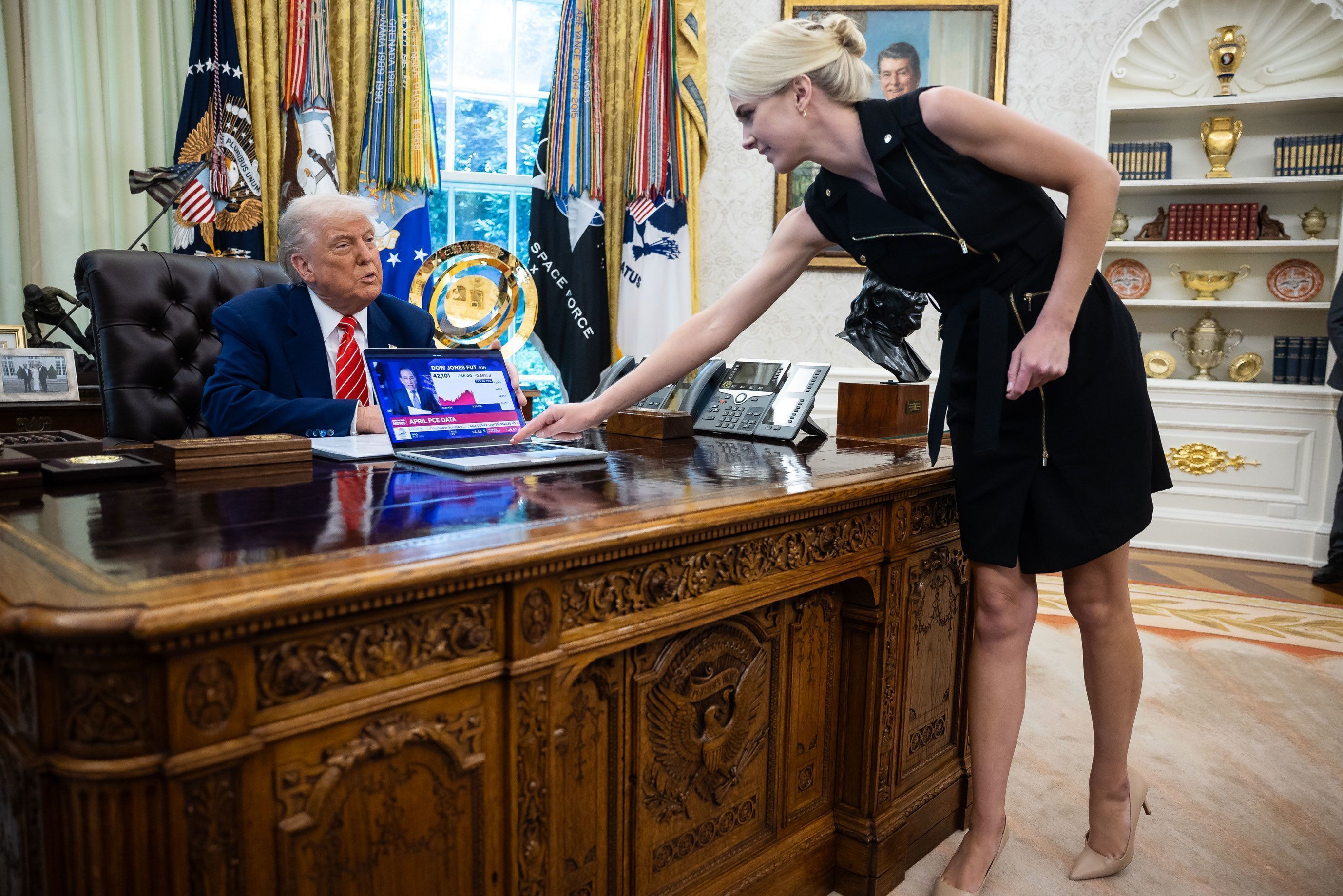 O presidente Donald Trump observa enquanto Natalie Harp, uma assessora, posiciona um computador que exibia uma reportagem sobre o mercado de ações durante uma coletiva de imprensa no Salão Oval da Casa Branca, em 30 de maio de 2025 • Francis Chung/Pool/Sipa USA via Newsource