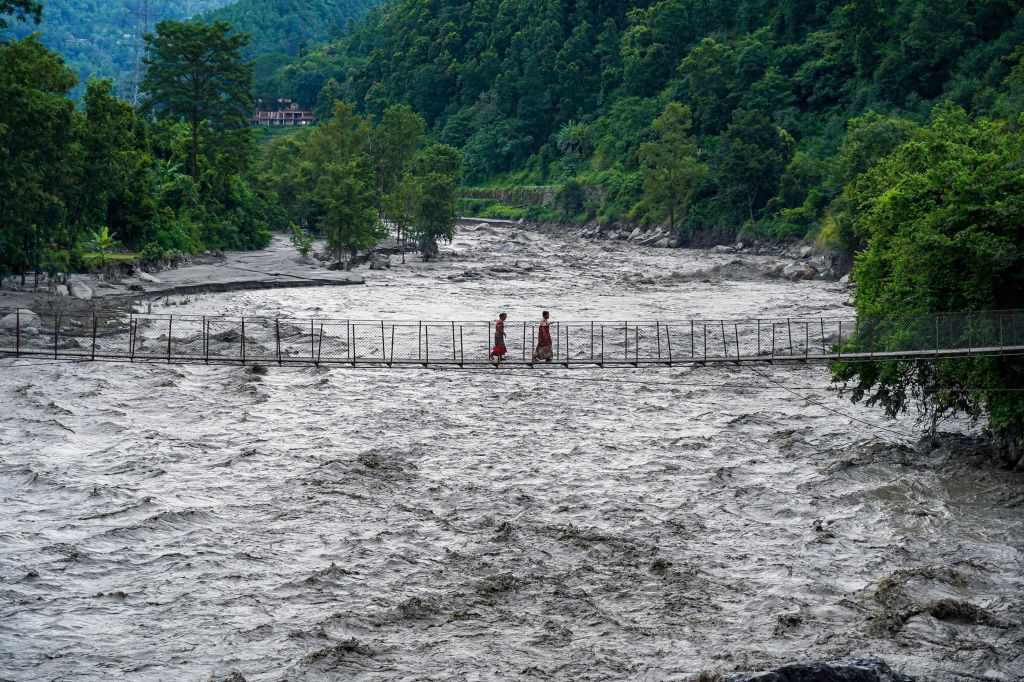 Pessoas caminham sobre uma ponte suspensa para atravessar o rio Trishuli, que está inundado, em Bhaise, Nuwakot, Nepal, em 8 de julho de 2025.