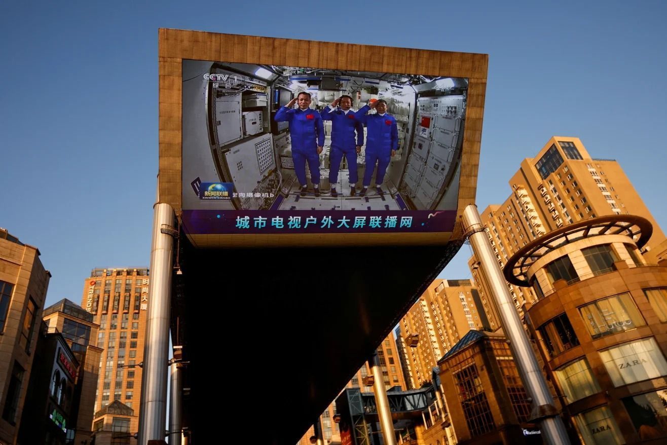Em um shopping center em Pequim, um telão gigante mostra taikonautas prestando continência dentro do módulo central Tianhe da estação espacial chinesa em 2021 • Thomas Peter/Reuters