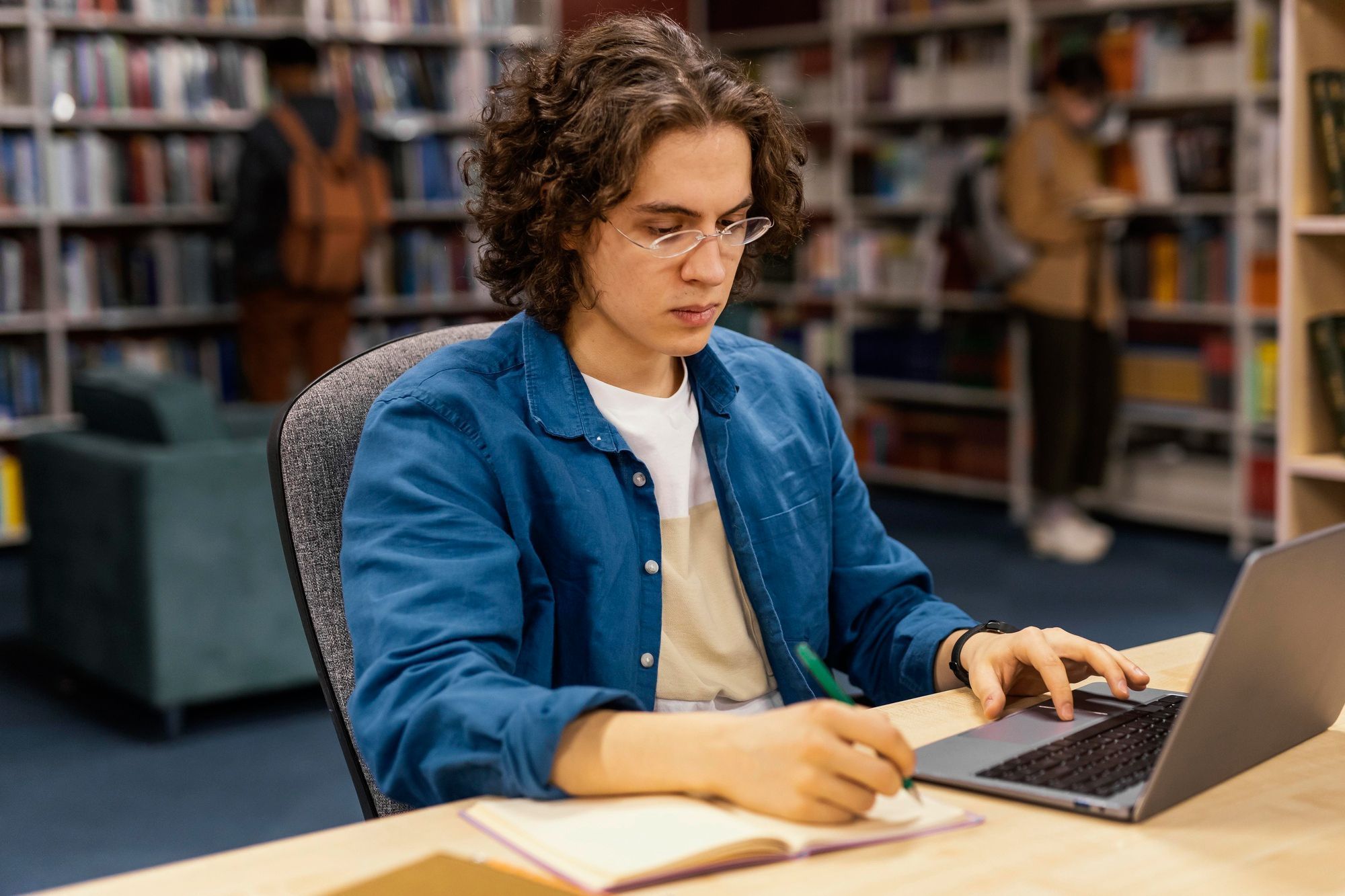 estudante-em-biblioteca-com-notebook-e-caderno-de-anotações