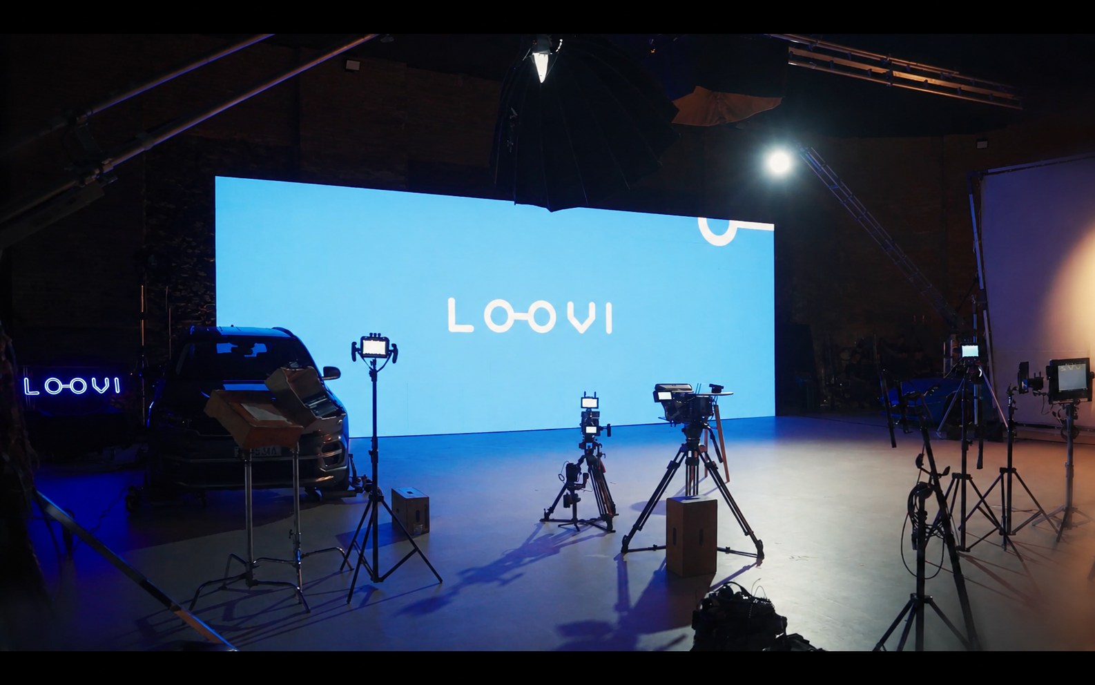 Estúdio de produção da Loovi com carro, câmeras e logotipo da empresa exibido em painel ao fundo.