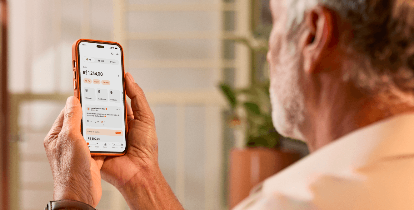 Homem de barba branca posicionado de perfil segurando à altura dos olhos um smartphone com o app do Inter aberto